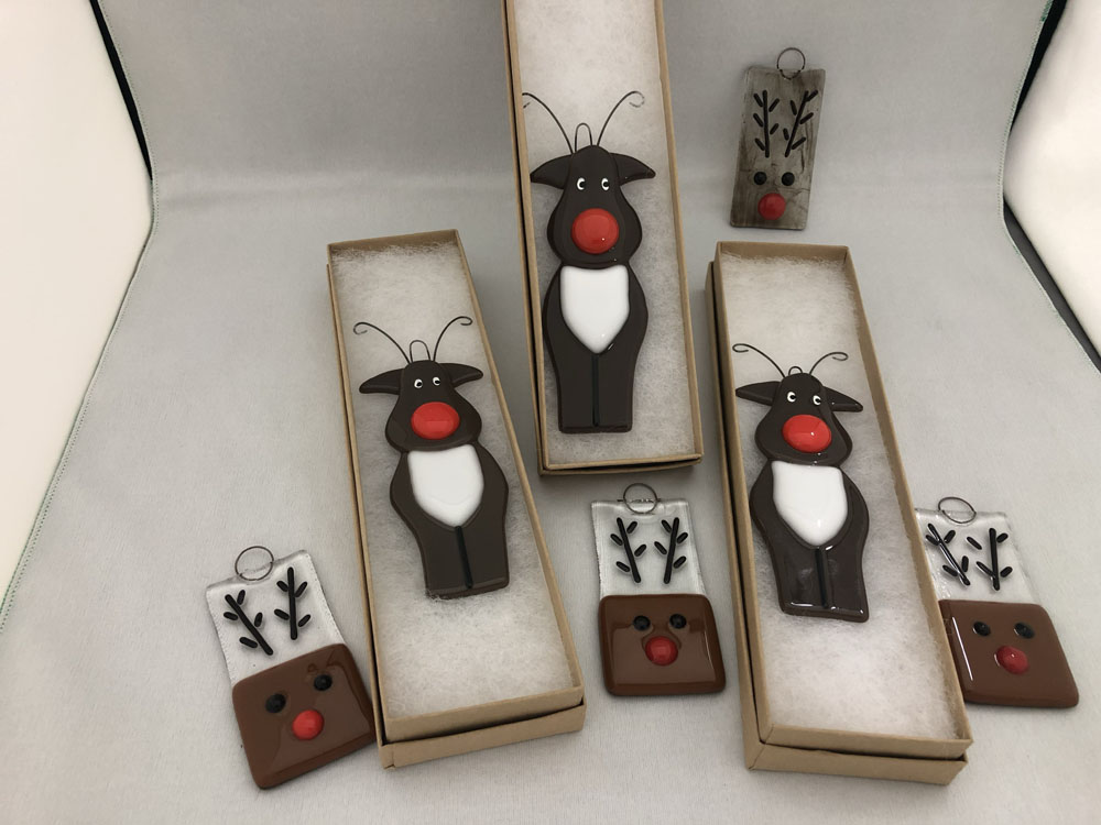 A set of fused glass reindeer ornaments, including stylized reindeer with large red noses and minimalist reindeer faces with antlers.